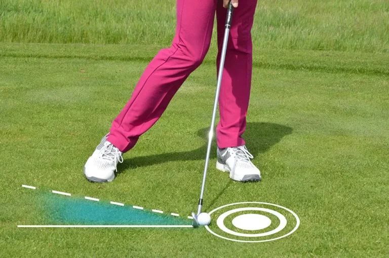 Golf player in pink pants swinging golf club on course; white shoes, target lines on grass